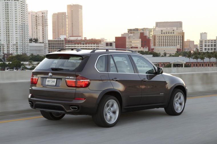 Driving 2013 BMW X5 xDrive50i in Sparkling Bronze Metallic from a rear right three-quarter view
